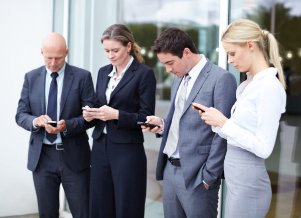 Group of four male and female executives using their cellphones outside their office.